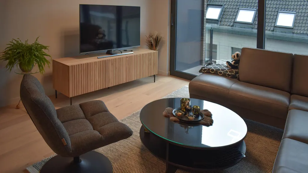 Coin salon aménagé avec des murs aux teintes douces, un meuble TV en bois et de grandes fenêtres à De Paulientjes.