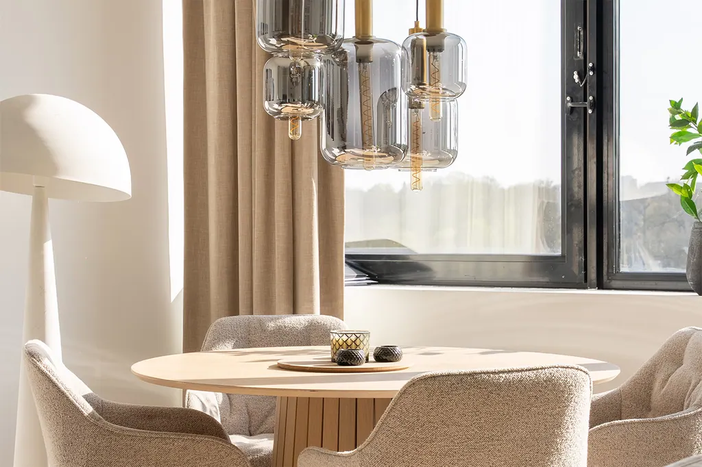 Suspensions en verre au-dessus d’une table à manger près de rideaux beiges dans un appartement témoin d’Artone.